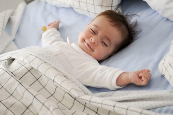 Smiling baby girl lying on a bed sleeping on blue sheets | مستشفى الأطباء المتحدون | جدة | احجز الآن